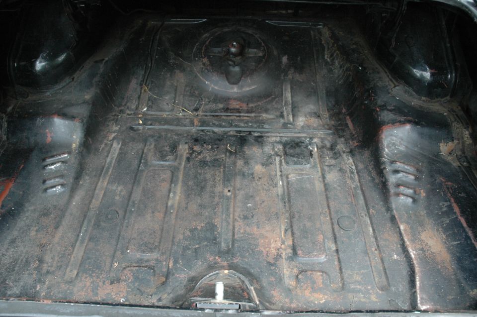 Empty car trunk floor pan, dirty and rusty bare steel with spare tire mount