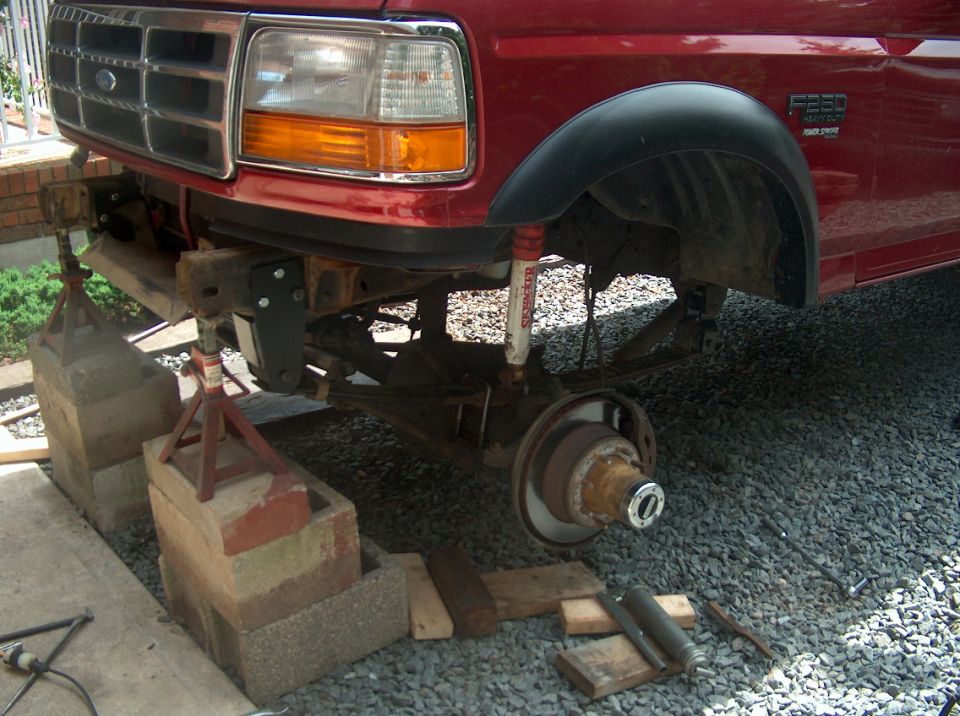 Red Ford F-250 front raised on jack stands and cinder blocks, wheel removed exposing brake rotor and hub.