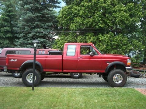 1996 Ford F-250 - A red crew cab pickup truck is parked in front of a residential setting with trees in the background.