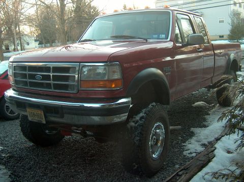 1996 Ford F-250 - This red 1996 Ford F-250 pickup truck is shown from a three-quarter front angle, lifted with large tires.