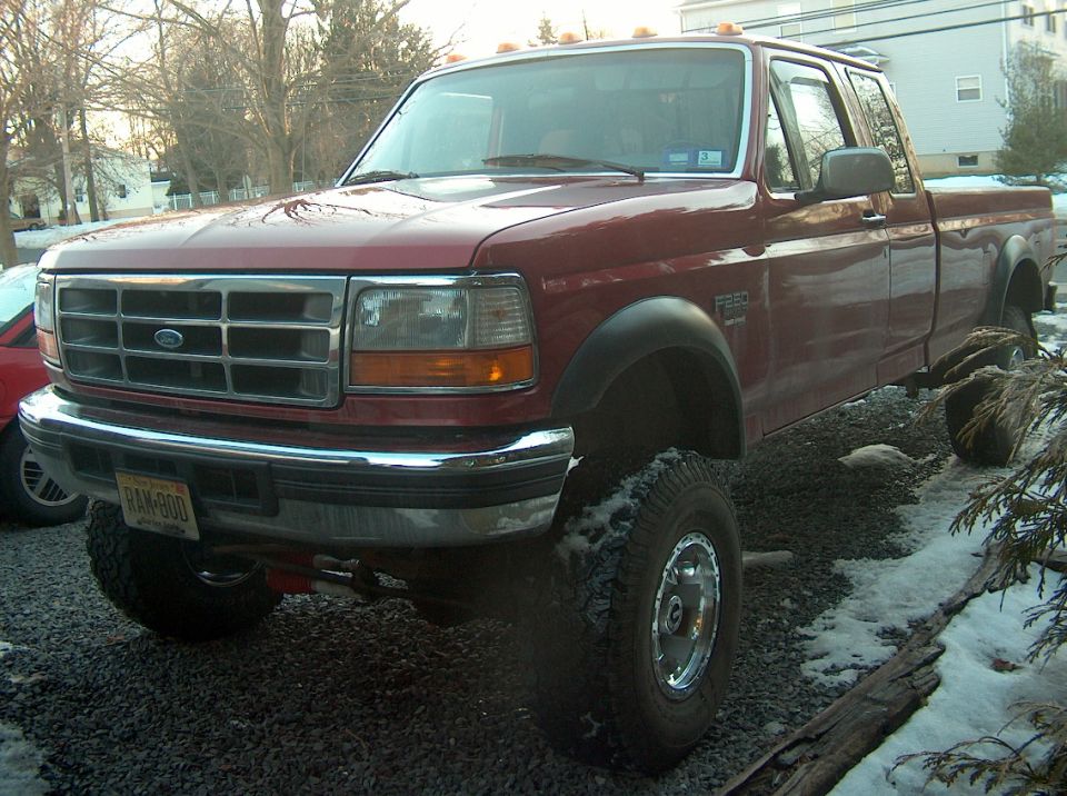 Red 1996 Ford F-250 pickup truck, lifted, with chrome grille and bumper, parked on gravel