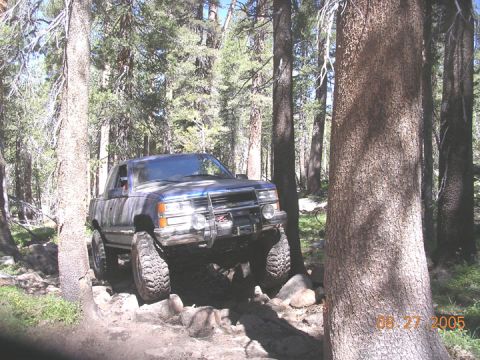 1994 Ford Bronco - Pickup truck driving off-road through a forest on a rocky path. Date stamp: 08.27.2005.