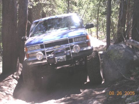 1994 Ford Bronco - A blue off-road truck navigates a rocky trail, kicking up dust.