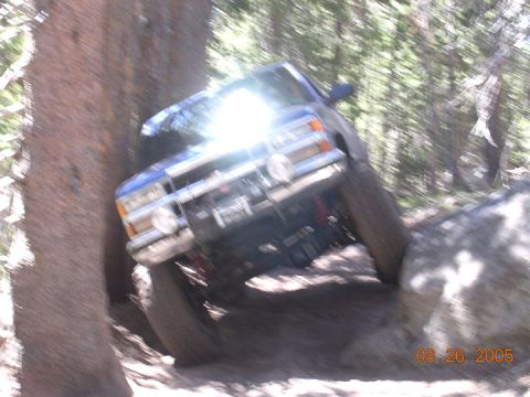 1994 Ford Bronco - A blue off-road truck navigates a rocky trail with trees on either side.