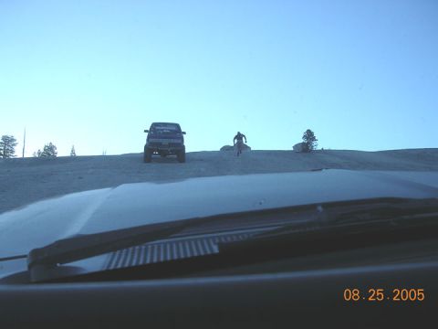 1994 Ford Bronco - A lifted pickup truck is parked on a sandy incline with a person walking nearby, as seen from the interior of another vehicle.