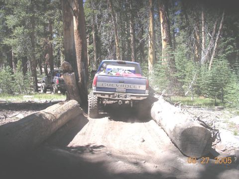 1994 Ford Bronco - A Chevrolet pickup truck navigates a challenging off-road course through a wooded area, with another vehicle in tow.