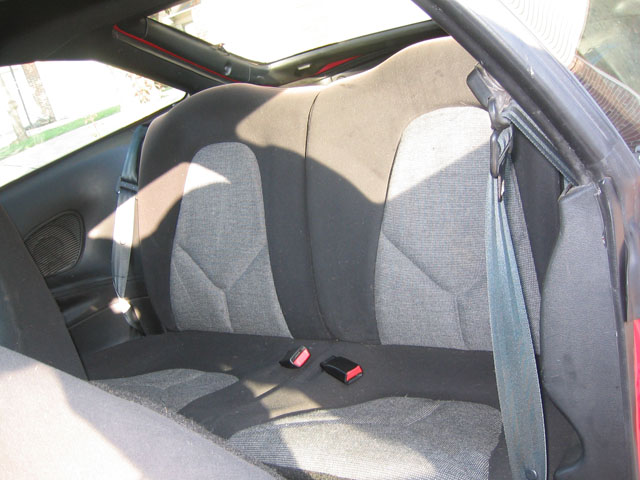 Gray cloth rear seat inside a coupe with seatbelt buckles and tinted side glass