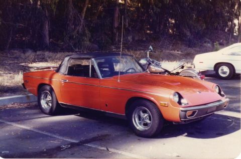 1991 Ford Taurus - This orange sports car is parked next to a white sedan in a lot.