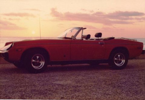 1991 Ford Taurus - A red Jensen-Healey GT convertible is parked near the water with a colorful sky in the background.