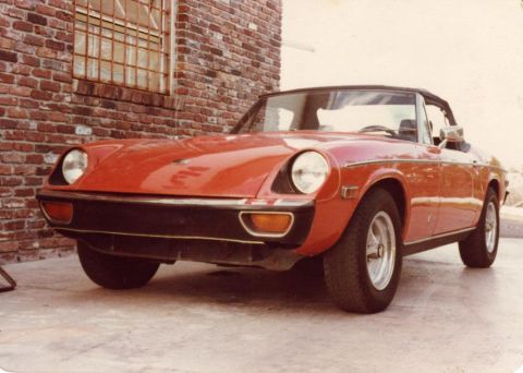 1991 Ford Taurus - A red convertible sports car is parked outdoors next to a brick building.