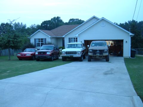 1983 Ford Bronco - Several vehicles are parked in a driveway in front of a suburban house.