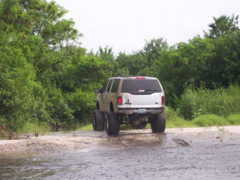 2000 Ford Excursion - Rear view of a lifted 2000 Ford Excursion with oversized tires navigating through a wet, muddy area.