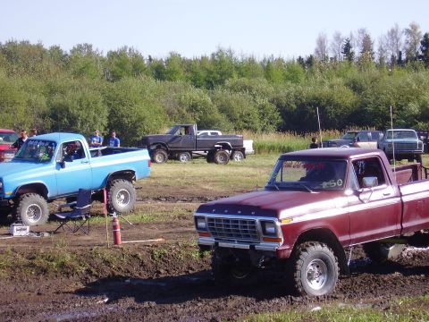 1979 Ford F-250 - A maroon 1979 Ford F-250 sits in the mud next to a blue pickup truck, with other vehicles in the background.