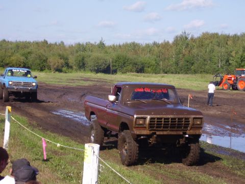 1979 Ford F-250 - Mud-covered 1979 Ford F-250 navigates a muddy track, with another truck and a tractor visible in the background.