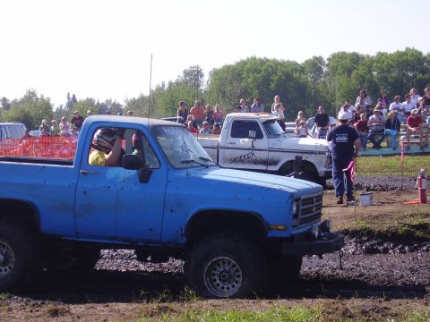 1979 Ford F-250 - A blue pickup truck navigates a mud race with a white truck behind it and a crowd watching.