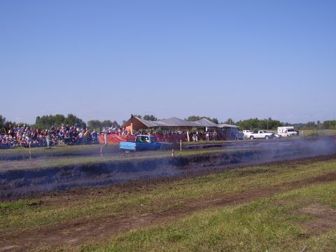 1979 Ford F-250 - A blue pickup truck competes in a mud race event, kicking up dirt and smoke.