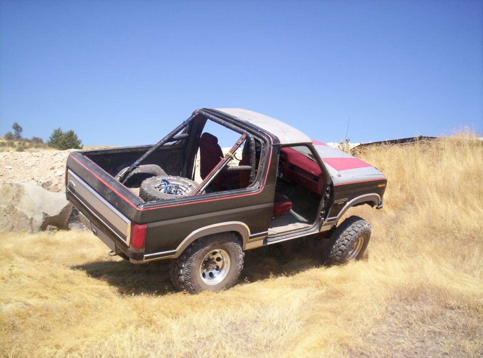 Rear quarter of a black and red topless lifted Ford Bronco in dry grass, hardtop removed nearby