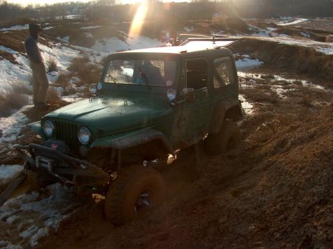 1996 Ford F-250 - A green Jeep navigates a challenging muddy terrain with a person observing nearby.