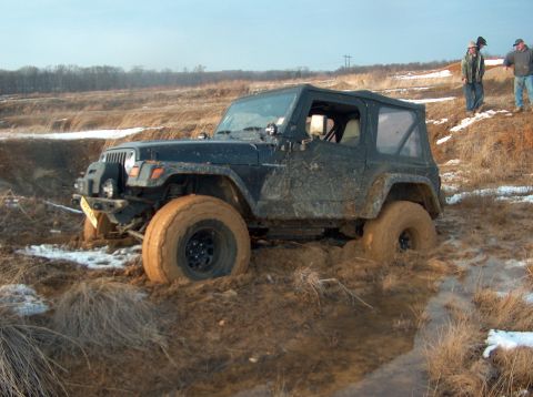 1996 Ford F-250 - A black Jeep Wrangler is stuck deep in mud, with two people observing from a nearby hill.