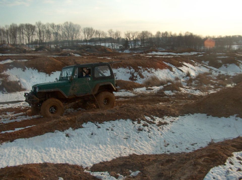 Green Jeep Wrangler driving through mud and snow on a dirt track