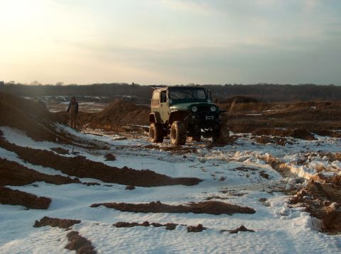 1996 Ford F-250 - A green Jeep Wrangler is parked in a snowy, muddy landscape under a hazy sky.