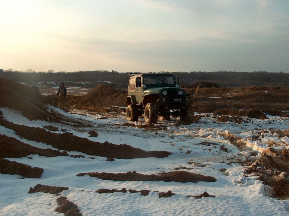 Green Jeep Wrangler parked on snowy dirt mounds with a person standing nearby