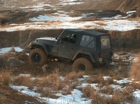 1996 Ford F-250 - A black Jeep Wrangler navigates a challenging muddy off-road course with snow and dry vegetation.