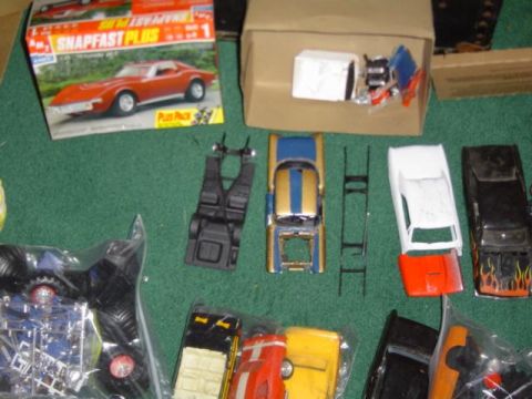 1979 Ford Bronco - Various model car kits and unassembled parts are laid out on a green surface, including a monster truck chassis and several car bodies.