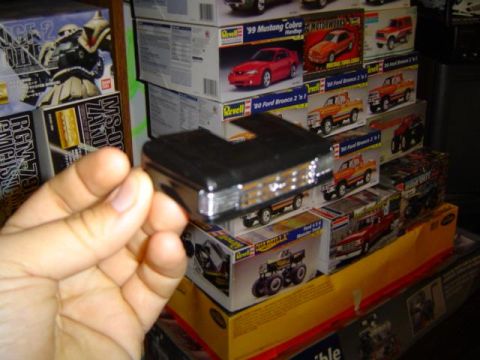 1979 Ford Bronco - A hand holds a black model car grille with chrome detailing, surrounded by model car boxes.