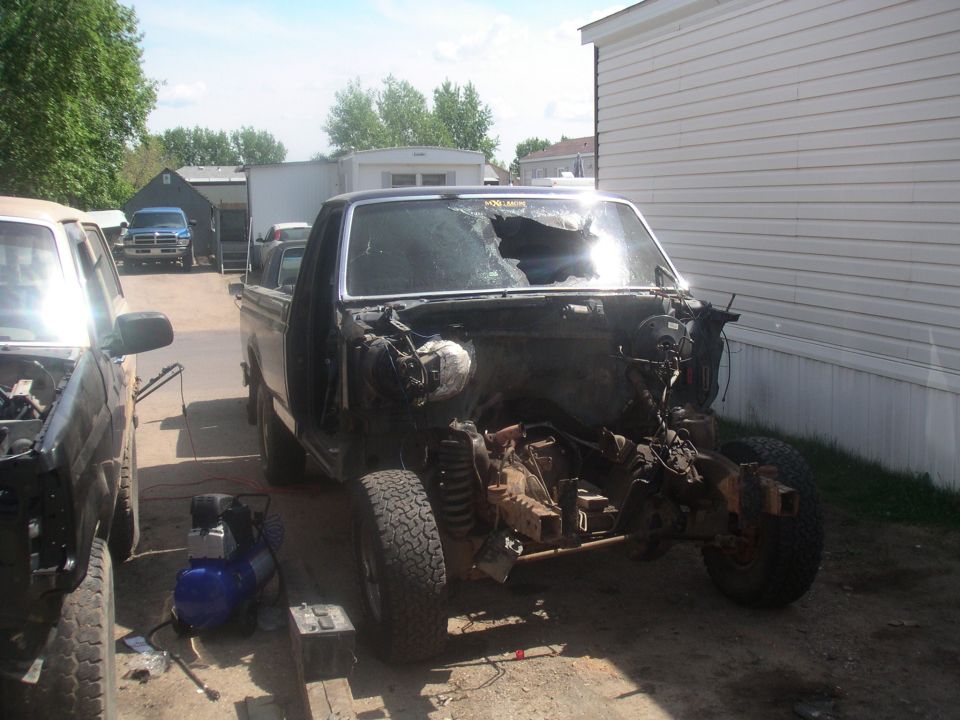 Partially dismantled dark Ford truck with front clip and engine removed and smashed windshield