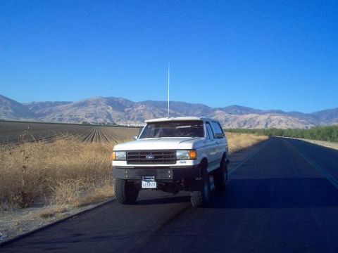 1988 Ford Bronco - A white Ford Bronco is parked on the shoulder of a road with fields and mountains visible.