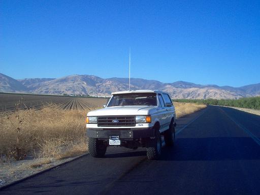 White Ford Bronco parked on the side of a rural road with mountains in the background