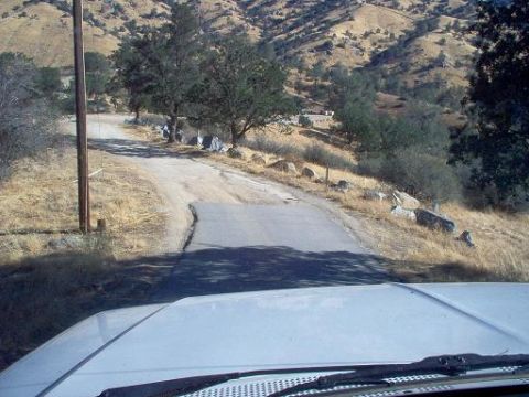 1988 Ford Bronco - View from inside a white vehicle driving on a dusty road through a dry, hilly landscape.