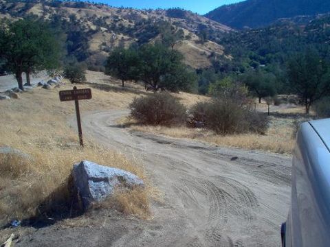 1988 Ford Bronco - A dirt road winds through a dry, hilly landscape with a signpost in the foreground.