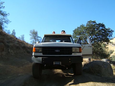 1988 Ford Bronco - A white Ford F-Series truck is parked on a dirt road with two people visible in the cab.