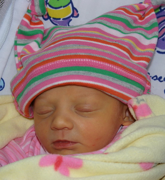 Newborn baby wearing a pink, green, and orange striped hat and yellow blanket