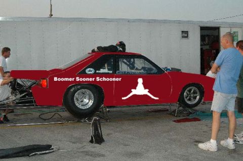 2005 Ford Mustang - A red drag car with custom decals is shown from the side, with people standing nearby.