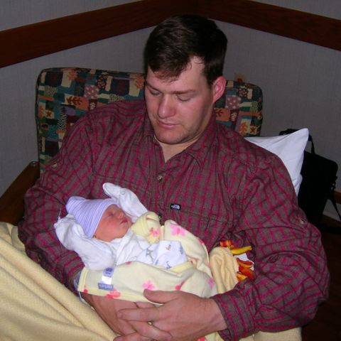 2003 Jeep TJ - A man cradles a newborn baby, who is swaddled in a blanket and wearing a hat.