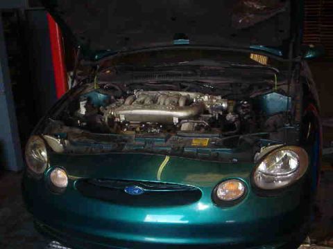 1997 Ford Taurus - The engine bay of a green sedan is visible with the hood up. A Ford logo is present on the grille.