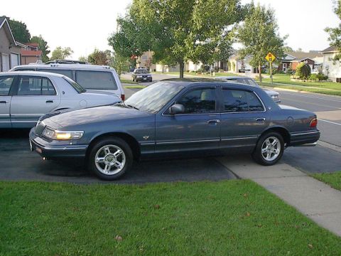 1985 Mercury Grand Marquis - A dark blue sedan is parked on a driveway in front of a residential house.