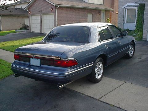1985 Mercury Grand Marquis - This blue sedan is parked in a suburban driveway, showing its rear three-quarter profile.