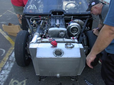 1990 Nissan Sentra - The exposed engine bay of a custom race car features a large turbocharger and an aluminum fuel tank, with mechanics working on the vehicle.