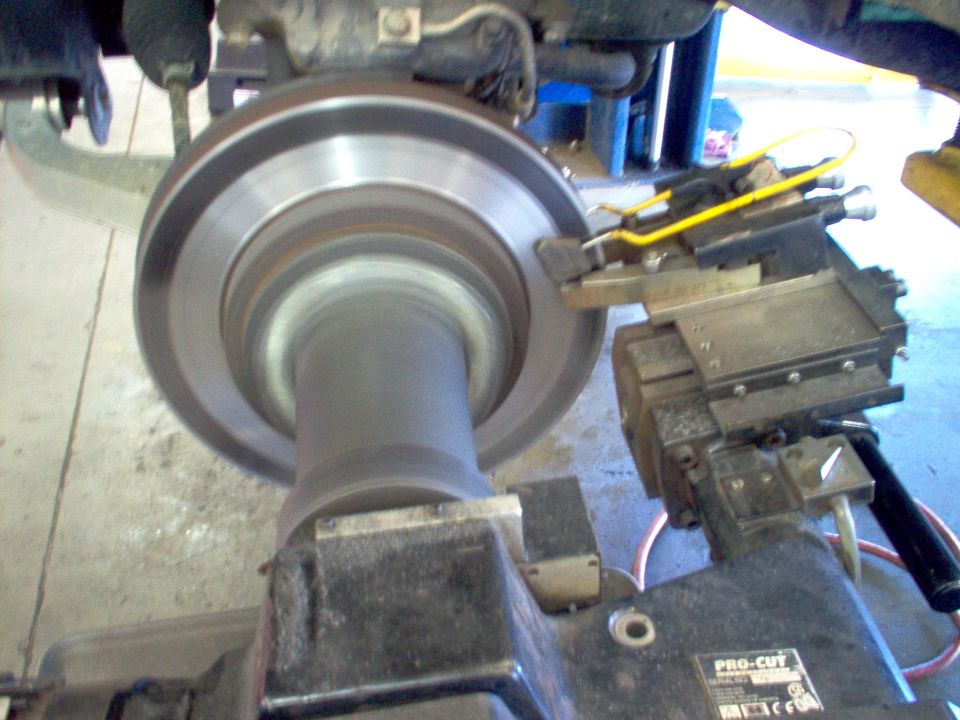 Brake rotor spinning on an on-car lathe under a lifted vehicle, cutting head engaged