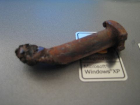 1990 Ford Bronco - heavily rusted, corroded curved metal part rests on a gray laptop bearing a Designed for Windows XP sticker.