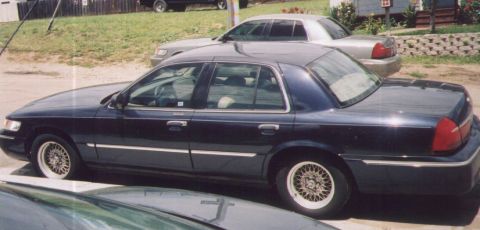 2000 Mercury Grand Marquis - A dark blue 2000 Mercury Grand Marquis sedan is parked next to another vehicle.