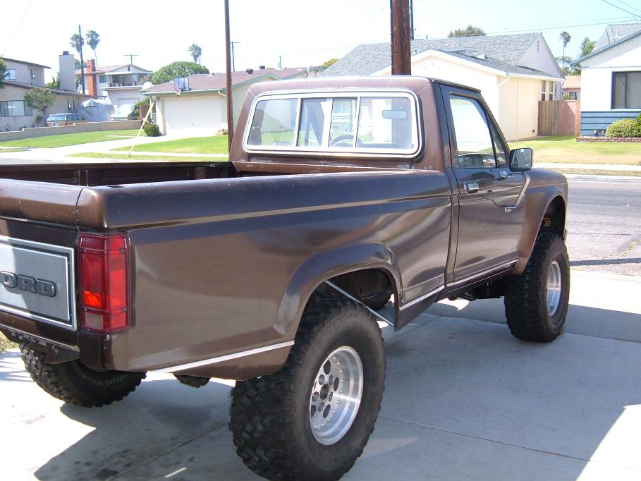 Brown Ford pickup truck, lifted with large tires, seen from rear quarter angle