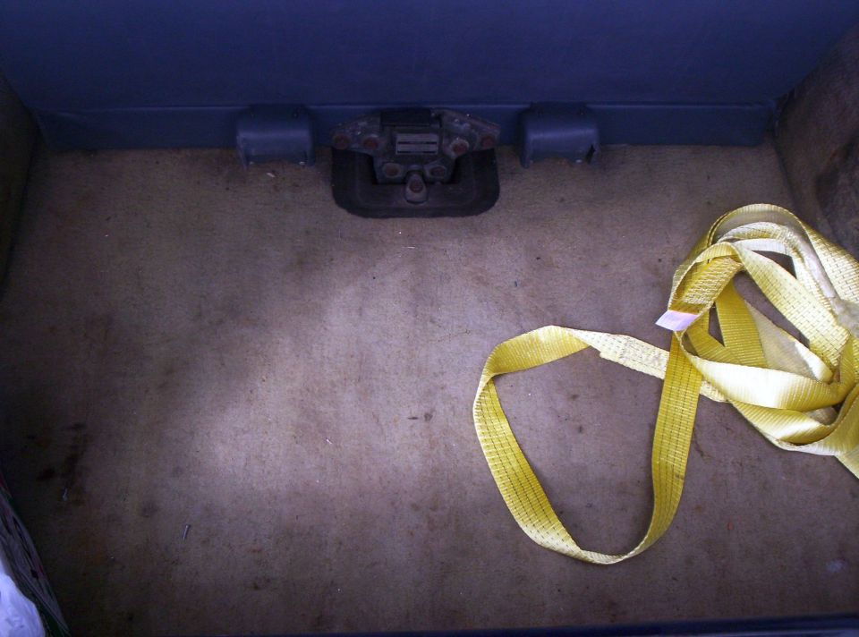 Cargo floor with tan carpet, blue trim, rusty tailgate latch, and coiled yellow strap