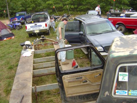 1987 Suzuki Samurai - A black Ford pickup truck cab and trailer are in the foreground, with other vehicles and tents in the background.