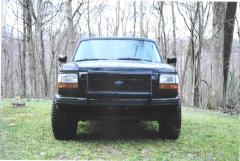 1992 Ford Bronco - This black Ford Bronco is parked in a grassy area with trees in the background.