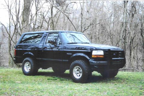 1992 Ford Bronco - Black 1992 Ford Bronco SUV with aftermarket grille guard parked on grassy area with trees in background.